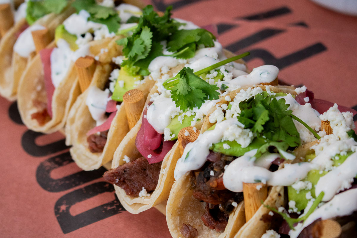 Carne asada street tacos topped with lime crema, charred salsa, cilantro, and pickled onions