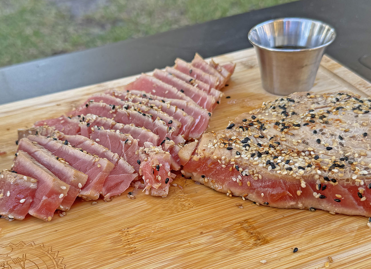 seared ahi tuna steaks cooked on pit boss gas griddle topped with sesame seeds, sliced on wooden cutting board