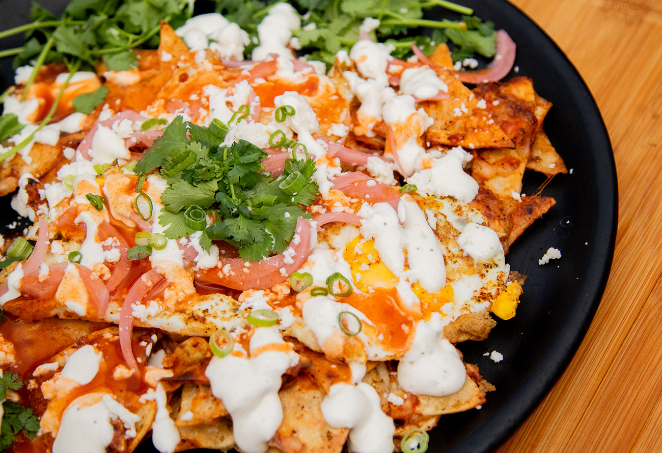 red sauce chilaquiles rojos with melted cheese, over easy eggs, garnished with sour cream, pickled onions and cilantro