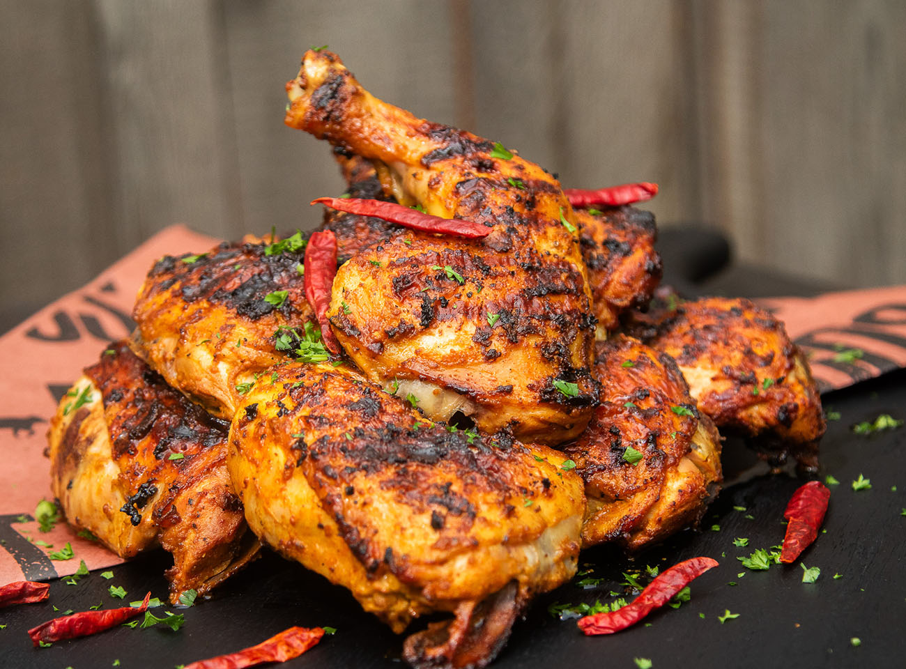 grilled tandoori chicken cooked on pit boss wood pellet grill and garnished with dried chilis and parsley, served on black platter